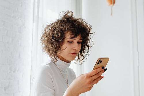 A woman in her forties looking drained while holding her phone in a bright room, showing what thin emotional boundaries feel like