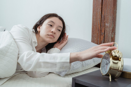 A woman lying awake in a bright modern bedroom with her eyes open, showing how stress and sleep interfere with each other at night
