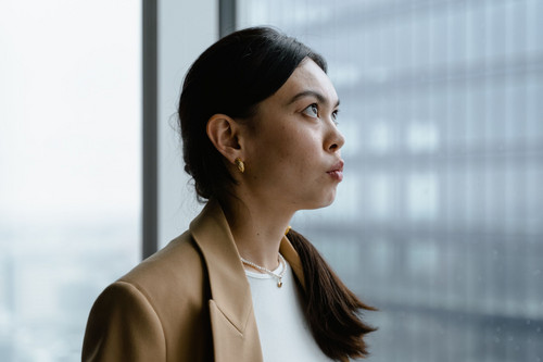 A woman in her forties standing by a bright window looking preoccupied, replaying the thought that mindset shifts can interrupt