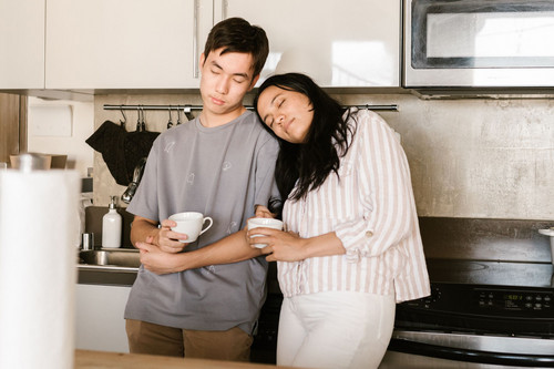 A tired woman in her forties leaning on a bright kitchen bench with a coffee, the groggy start that morning energy rituals are meant to change
