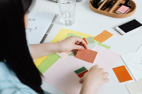 A woman holding bright paint samples against a wall in daylight, beginning to change her colour and mood at home