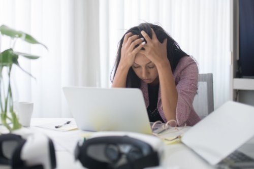 A woman in her forties looking tense at her laptop in a bright office, showing how remote work psychosocial risks go unnoticed