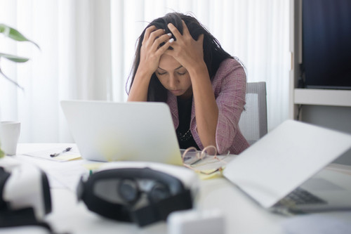 A woman in her forties looking tense at her laptop in a bright office, showing how remote work psychosocial risks go unnoticed