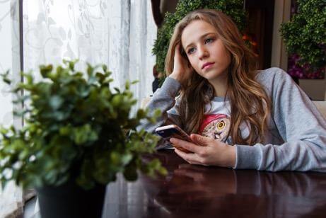 Girl on her phone at a table, looking sad.