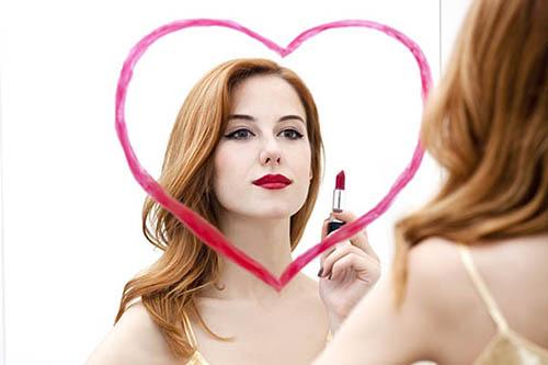 woman drawing a lipstick heart on a mirror