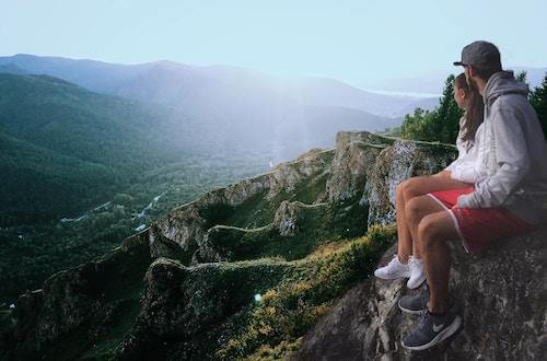 man, woman, sitting on a cliff watching the sunrise