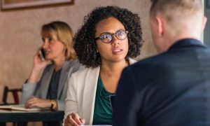 curly black hair woman sits in coffee shop seriously talking to college