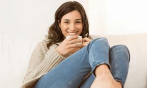 woman sitting on white couch holding white mug smiling