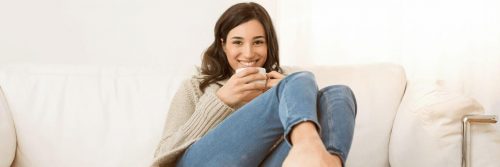 woman sitting on white couch holding white mug smiling
