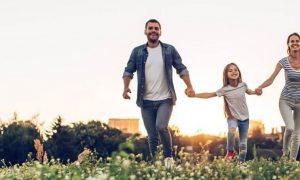 parents hold daughter hands happily walking on field smiling in sunny sky
