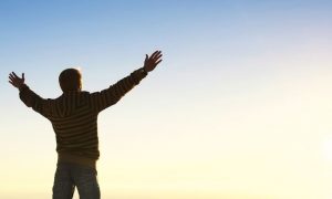 man stands alone raising hands feeling grateful about life in sunny blue sky