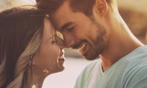 couple stands head to head happily smiling in sunny sky