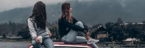 two young women sit on car top enjoy foggy weather gratitude life