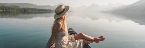 woman sits on boat in peaceful lake looking at mountain foggy sky