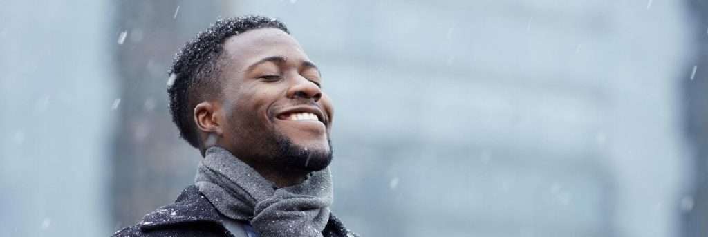 man wearing grey scarf happily smiles enjoys snow weather