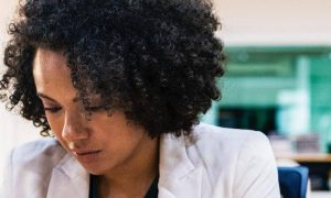curly black hair woman wearing white vest sits in office focusing on work