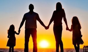 happy family stands hand in hand beside ocean sea cliff watching breathtaking sunset scene