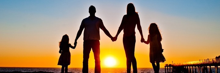happy family stands hand in hand beside ocean sea cliff watching breathtaking sunset scene