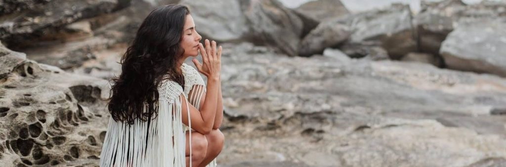 woman sits on rock eyes closed focusing on thinking breathing meditation in peaceful environment