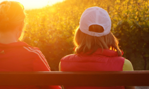 two women sits on bench facing backward watching sunset