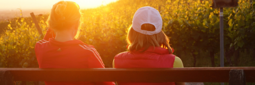 two women sits on bench facing backward watching sunset