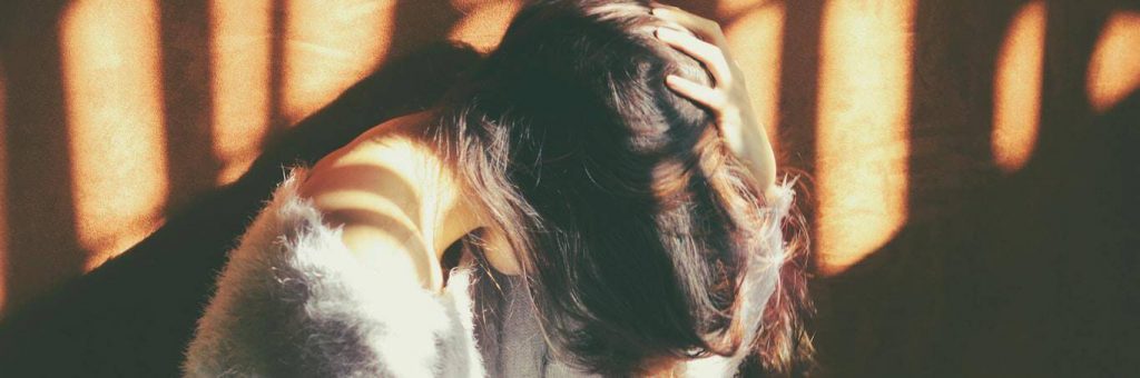 woman sits face down hand on hair feeling sad in dark place