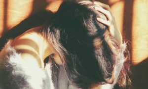 woman sits face down hand on hair feeling sad in dark place