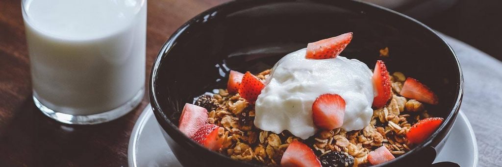 strawberry yogurt cereal breakfast bowl beside glass of milk