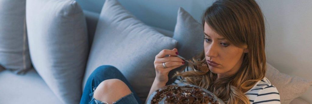 woman sits on couch sadly tiredly eating chocolate bowl