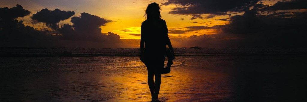 woman shadow approaches beach in dark sunset sky