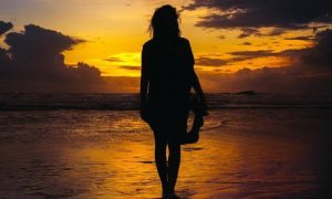 woman shadow approaches beach in dark sunset sky