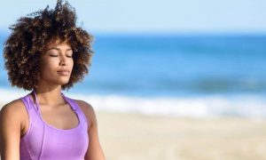 curly hair woman eyes closed meditate on beach in blue sky