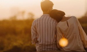couple sits watching sunset while woman lying on partner shoulder