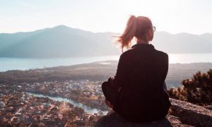 woman sits on rock enjoying nice weather looking at mountain blue sunny sky