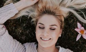 woman lies on grass eyes closed happily smiling gratitude life