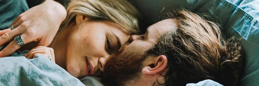 couple hugs lies on bed while man kissing on partner forehead