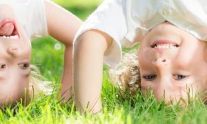 two girls stand heads on green field smiling having fun in park