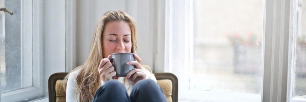 woman sits on chair holding grey mug enjoying drink in living room