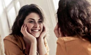 woman happily smiles looks herself in mirror