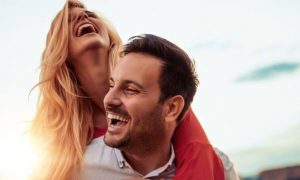 man carries girlfriend on back laughing while woman happily smiling