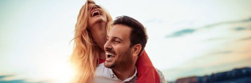 man carries girlfriend on back laughing while woman happily smiling