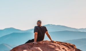 man sits on rock looking at mountain blue clear sky