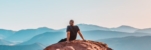 man sits on rock looking at mountain blue clear sky