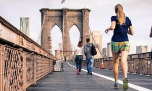 couple excitedly energetically exercises jogs along old bridge