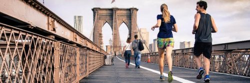 couple excitedly energetically exercises jogs along old bridge