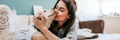 woman lies on bed hugging kissing puppy