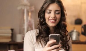 woman happily smiles using mobile phone in tidy living room