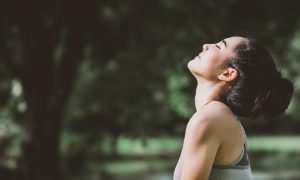 woman stands in forest eyes closed focuses on breathing practicing inner peace