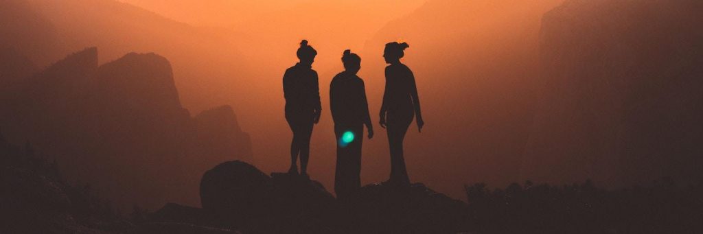 three women stand on rock in dark red sky