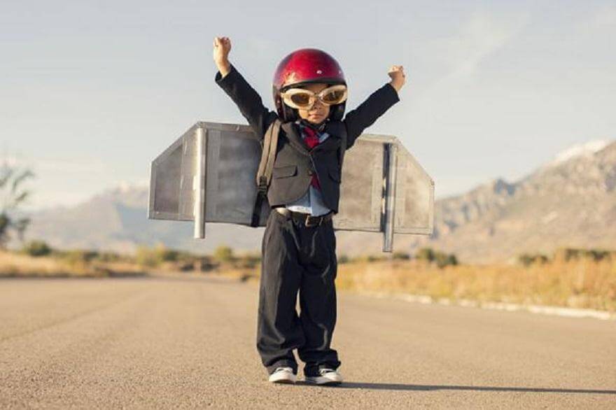 small kid stands alone raising hands carrying airplane designed bag